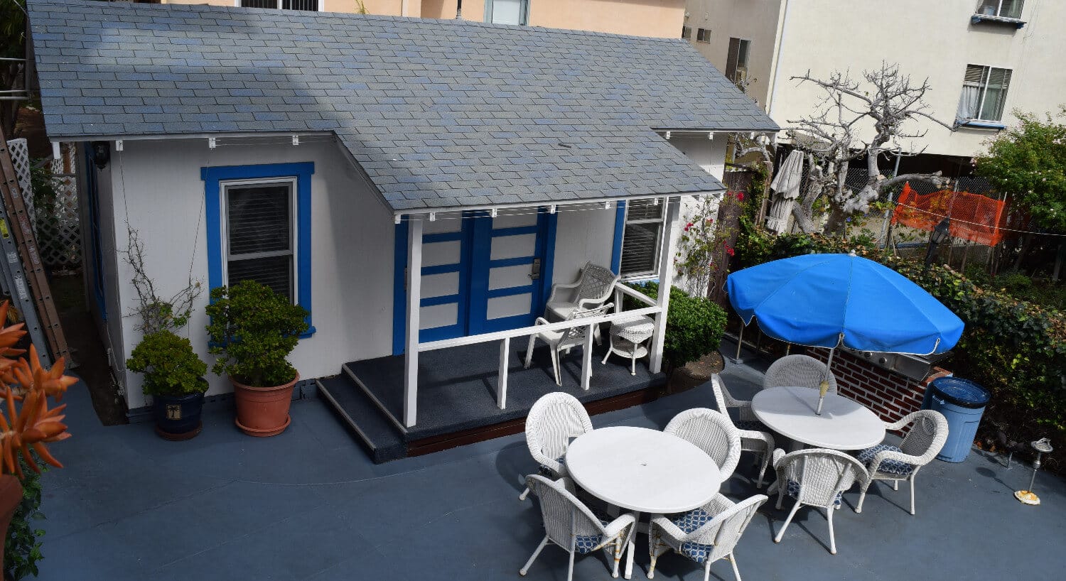 Ecterior of white cottage with blue trim with white patio tables and chairs. 