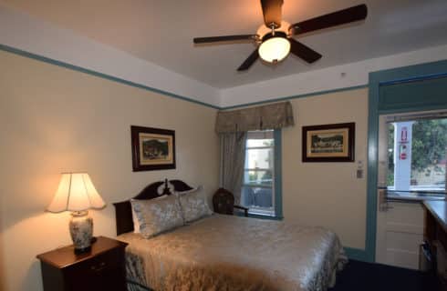 Bedroom with queen bed, wooden headboard an nightstand and a ceiling fan.