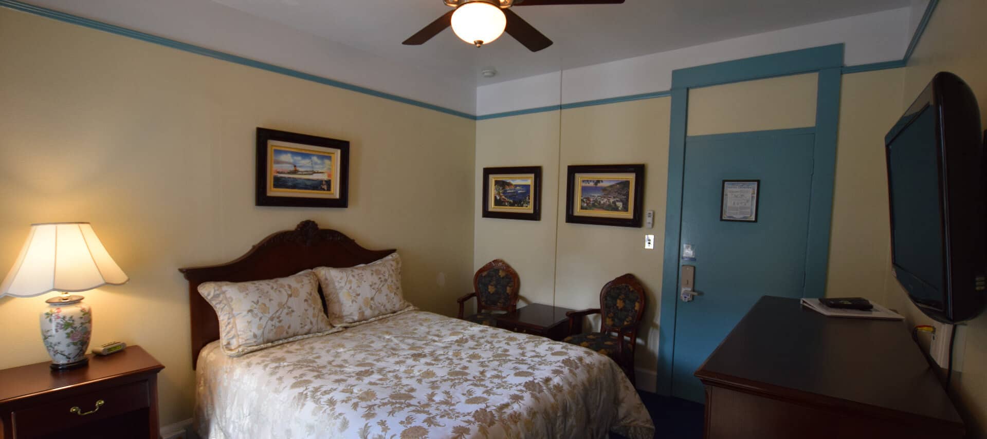 Room painted in yellow and bright blue with a queen bed and ceiling fan.